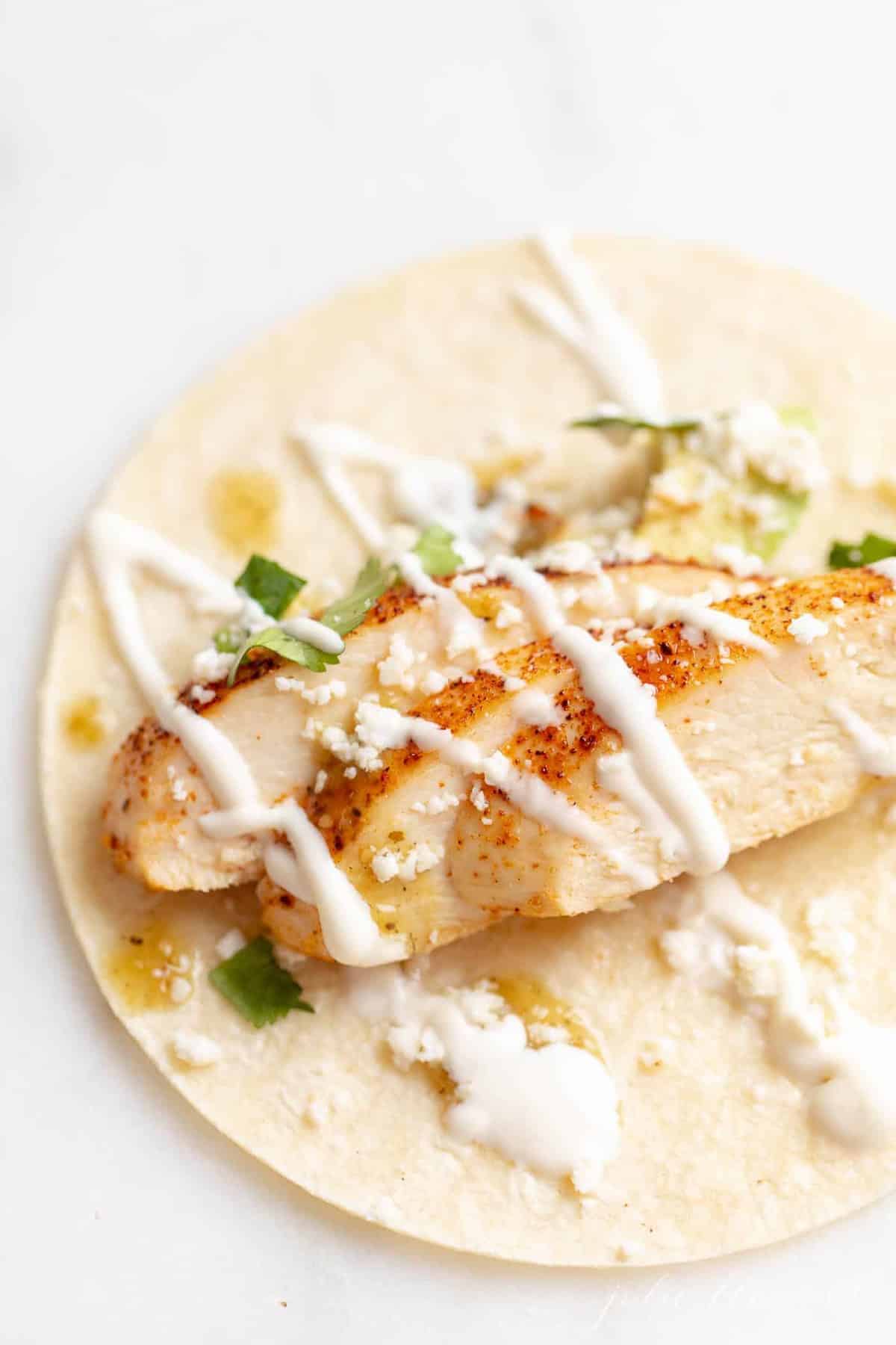 Close up of a corn tortilla filled with chicken soft taco ingredients.