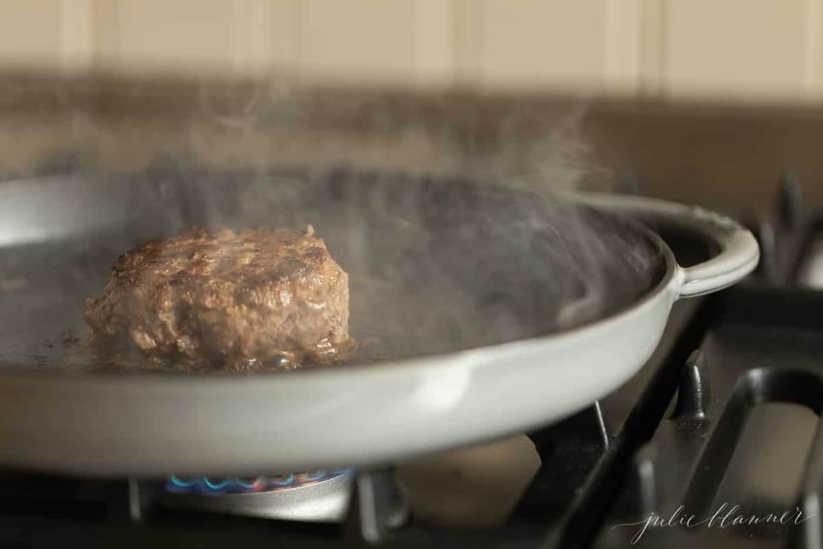 A cast iron pan, with a single juicy burger cooking inside.