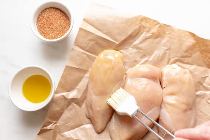 Raw chicken breasts being coated in melted butter before cooking.