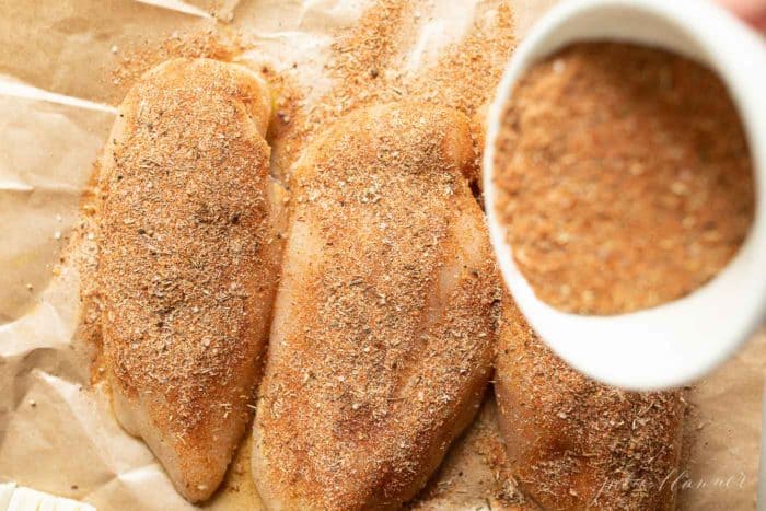 Raw Chicken breasts on brown butcher paper, covered in seasoning.