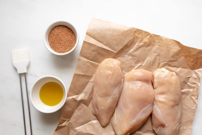 Raw chicken breasts on butcher paper, spices and melted butter to the side.
