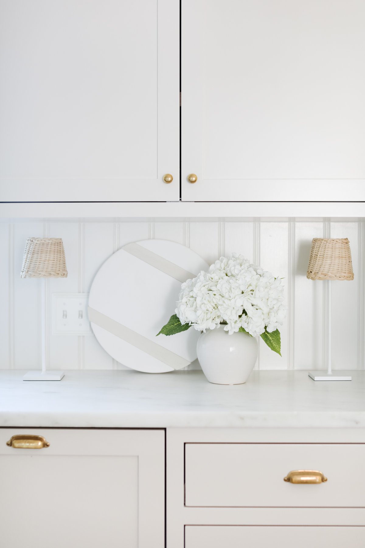 A classic white kitchen with white cabinets and a vase of flowers.