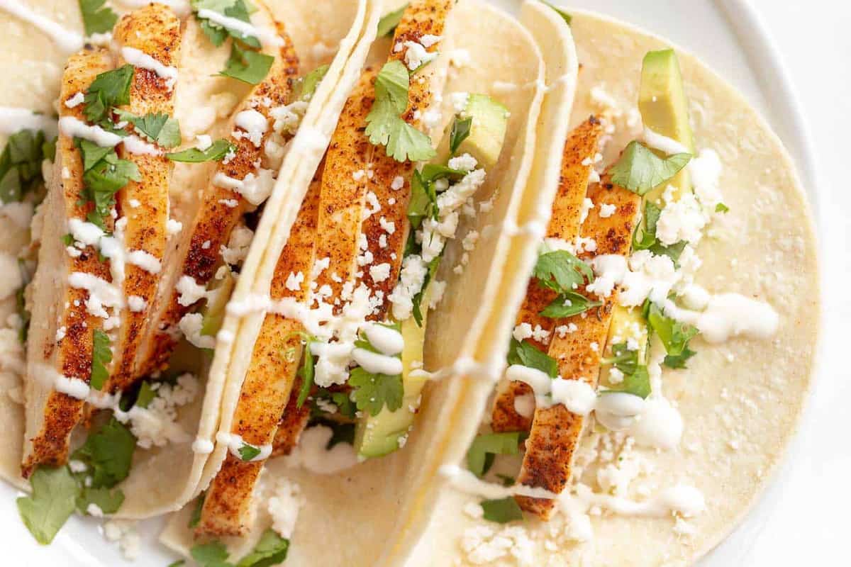 A white plate of three chicken soft tacos.