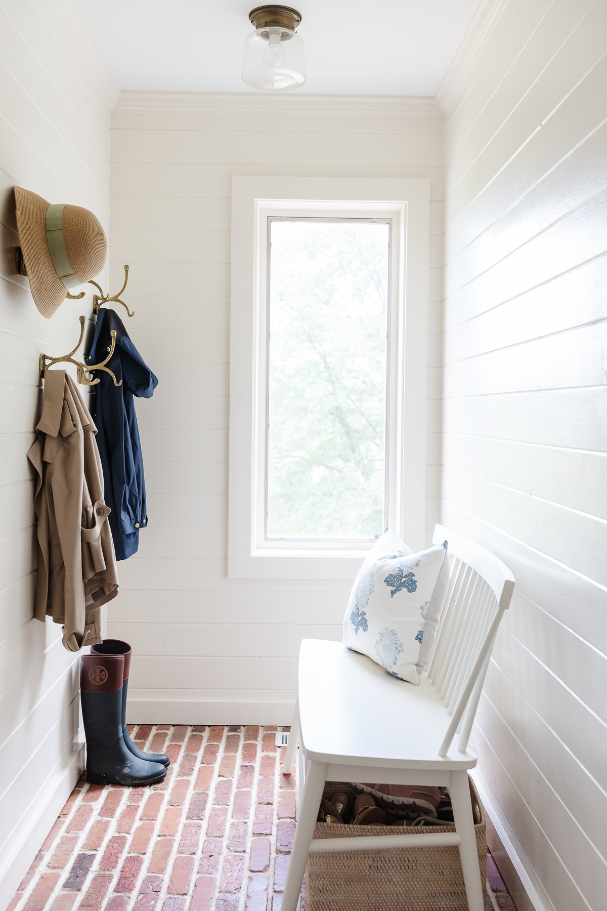 A white mudroom with brick floors and simple mudroom storage bench and hooks.
