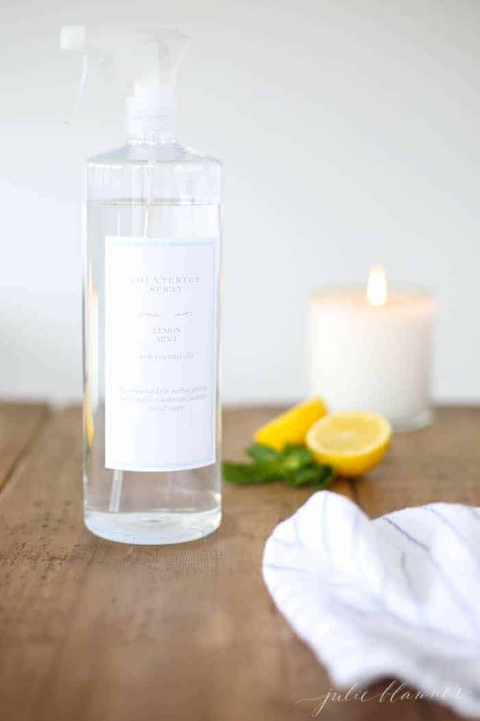 A clear glass spray bottle with a custom label, filled with natural all purpose organic cleaner - lemons and a candle in the background.