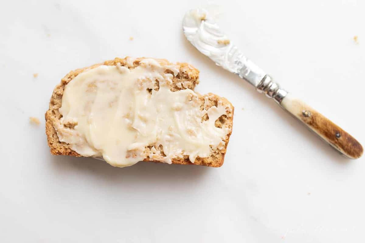 A slice of buttered bread, knife to the side, on a white marble surface.