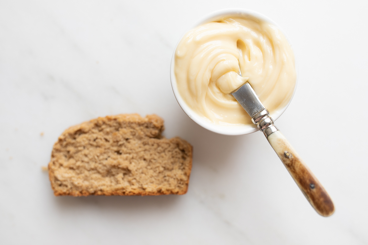 A small bowl of honey butter with a knife, next to a slice of bread.