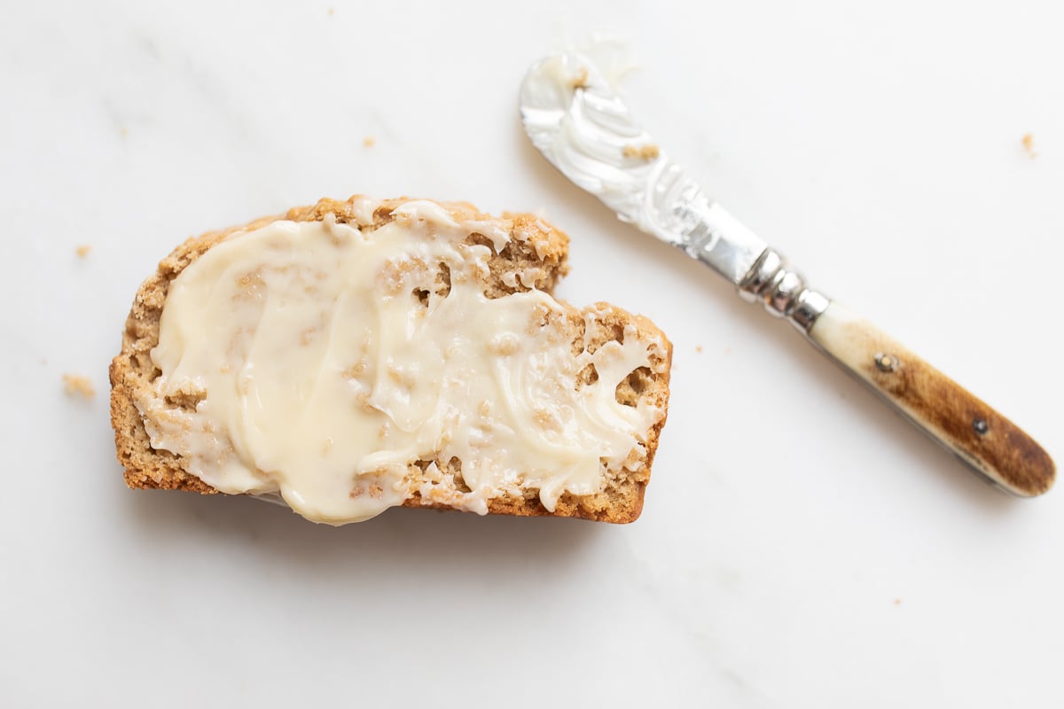 A slice of bread with honey butter across the top, knife above.