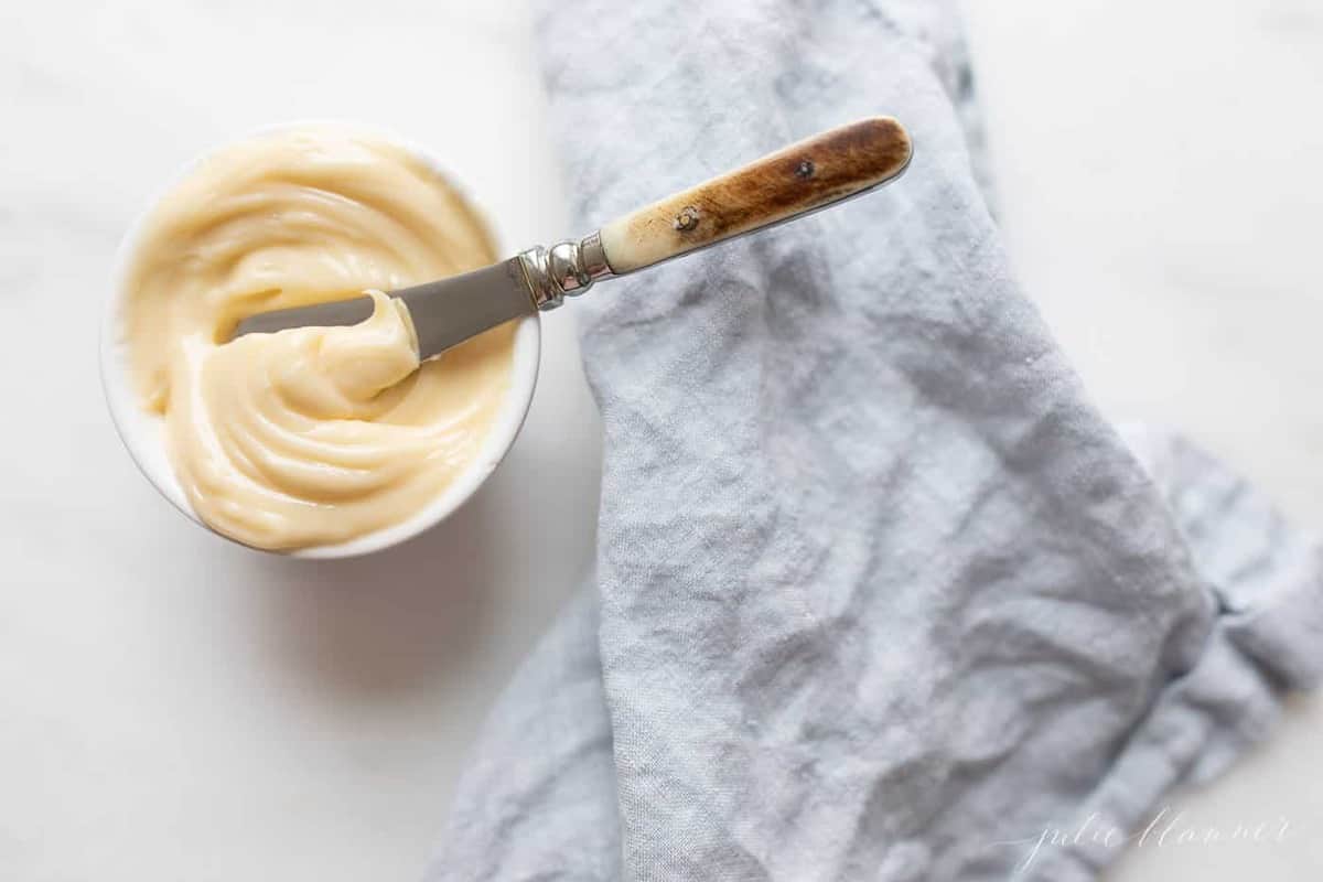 Creamy honey butter in a white bowl with a butter knife inside, and a blue linen napkin to the right. 