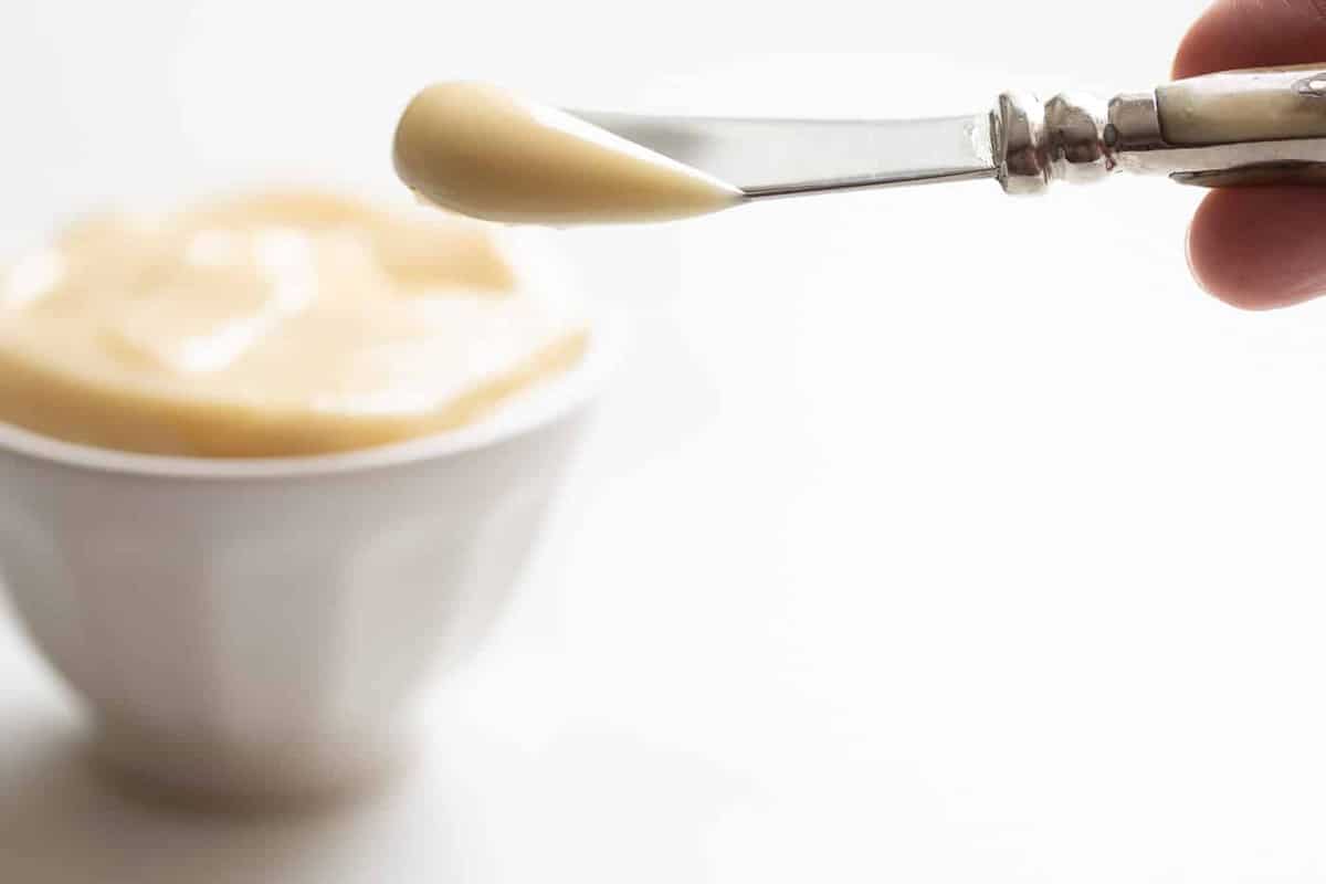 White surface, white bowl full of honey butter, knife coming out of bowl.