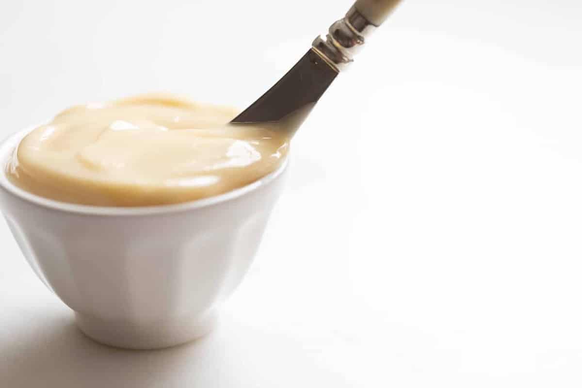 White surface, white bowl full of honey butter, knife inside bowl.