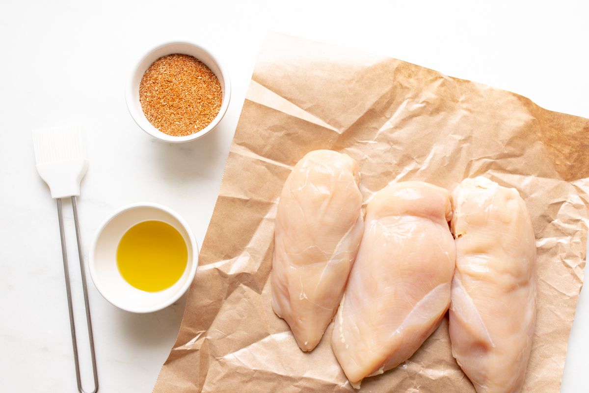 Raw chicken breasts with seasoning and butter nearby.