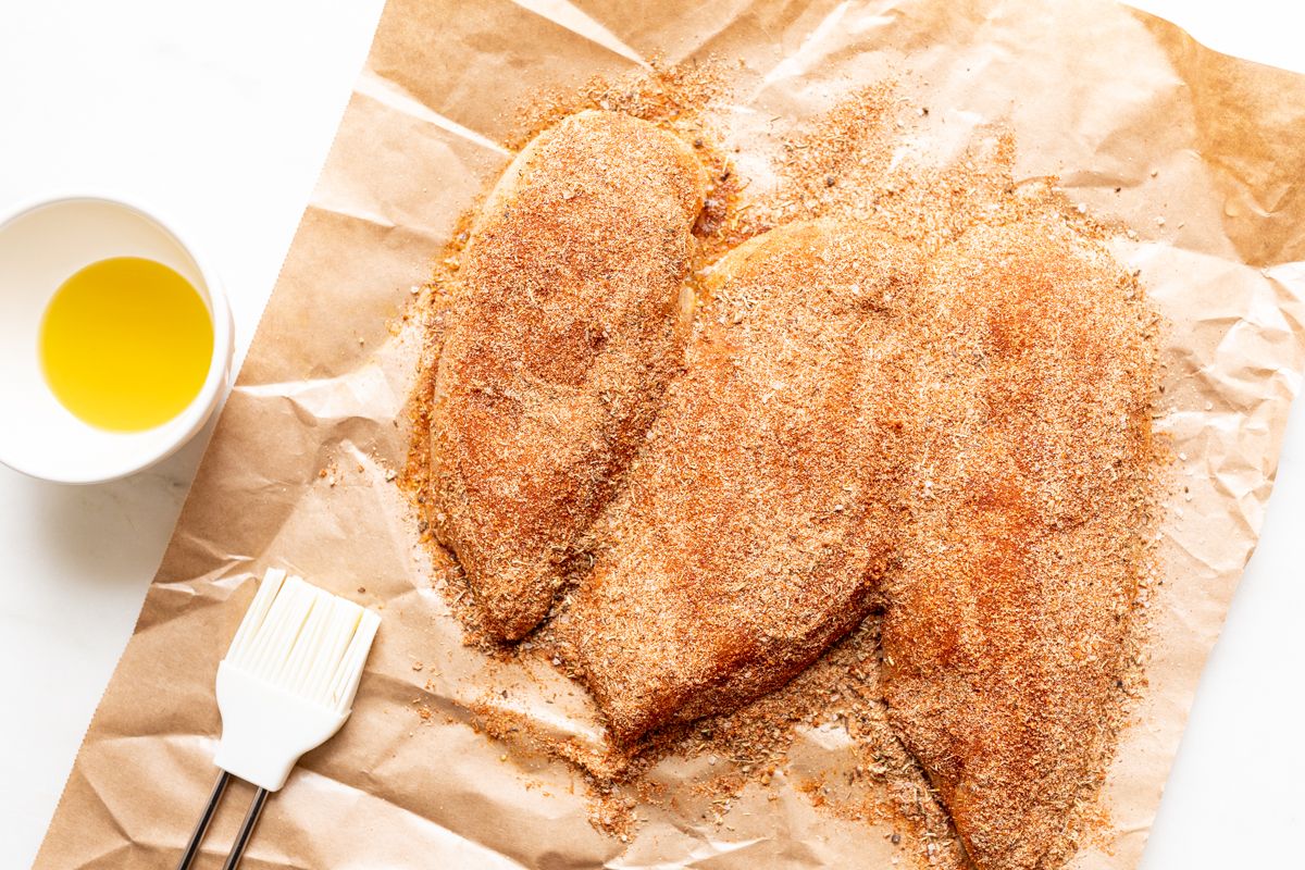 Raw chicken breasts on butcher paper, with butter and seasonings