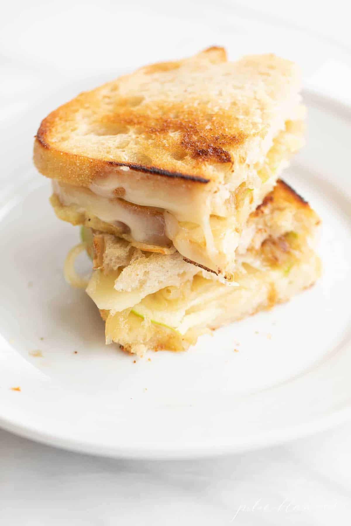 White plate with a sliced and stacked gourmet grilled cheese sandwich.