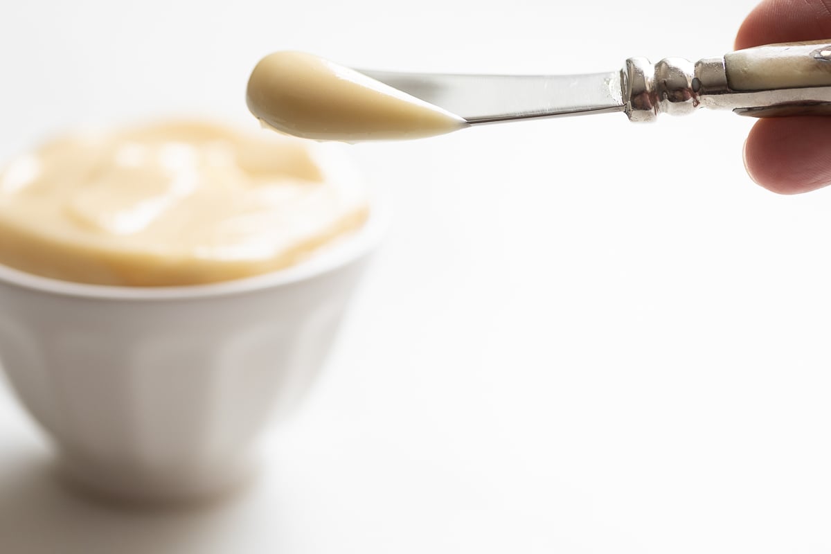 A knife with a pat of homemade honey butter, bowl of honey butter in the background