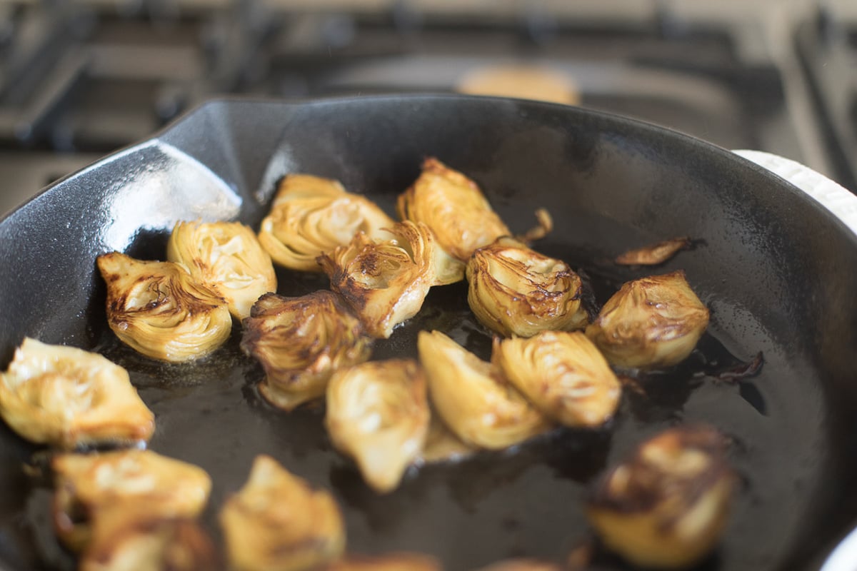 Fried artichokes in a saute pan on a stovetop.