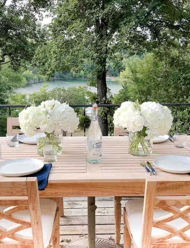 A wooden patio table set with hydrangea centerpieces, place settings, lake view in the background.