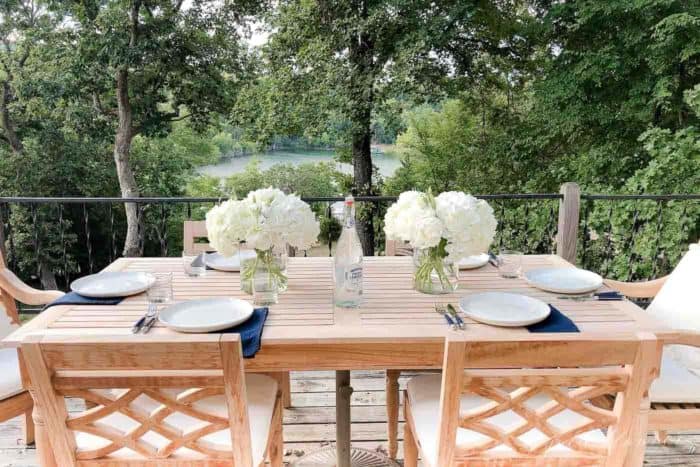 A wooden patio table set with hydrangea centerpieces, place settings, lake view in the background.