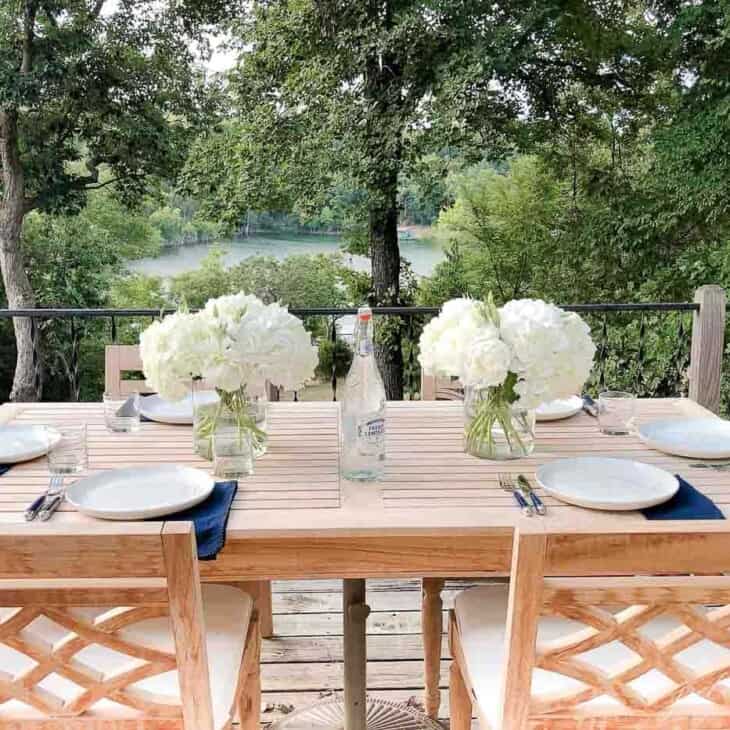 A wooden patio table set with hydrangea centerpieces, place settings, lake view in the background.