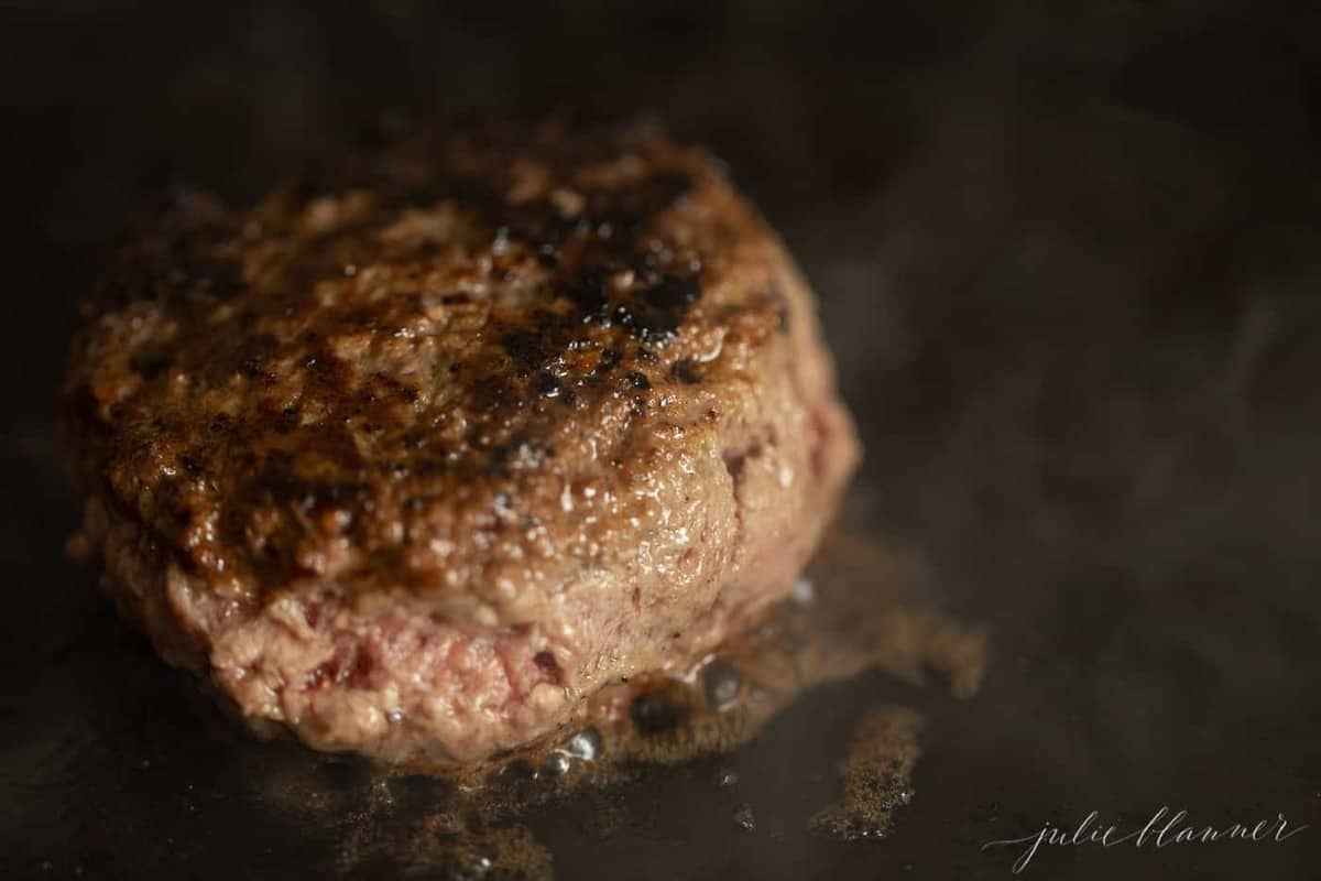 A cast iron pan, with a single juicy burger cooking inside.
