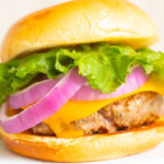 A juicy burger loaded with lettuce, red onion, and a beef patty nestled in a soft bun.