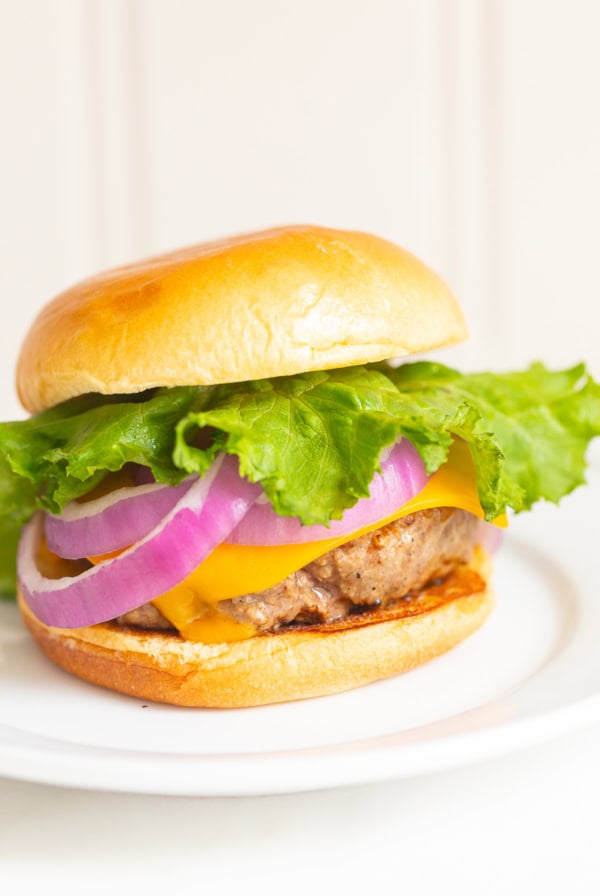 A juicy burger featuring lettuce, red onion slices, cheddar cheese, and a beef patty nestled in a bun, all elegantly presented on a white plate.