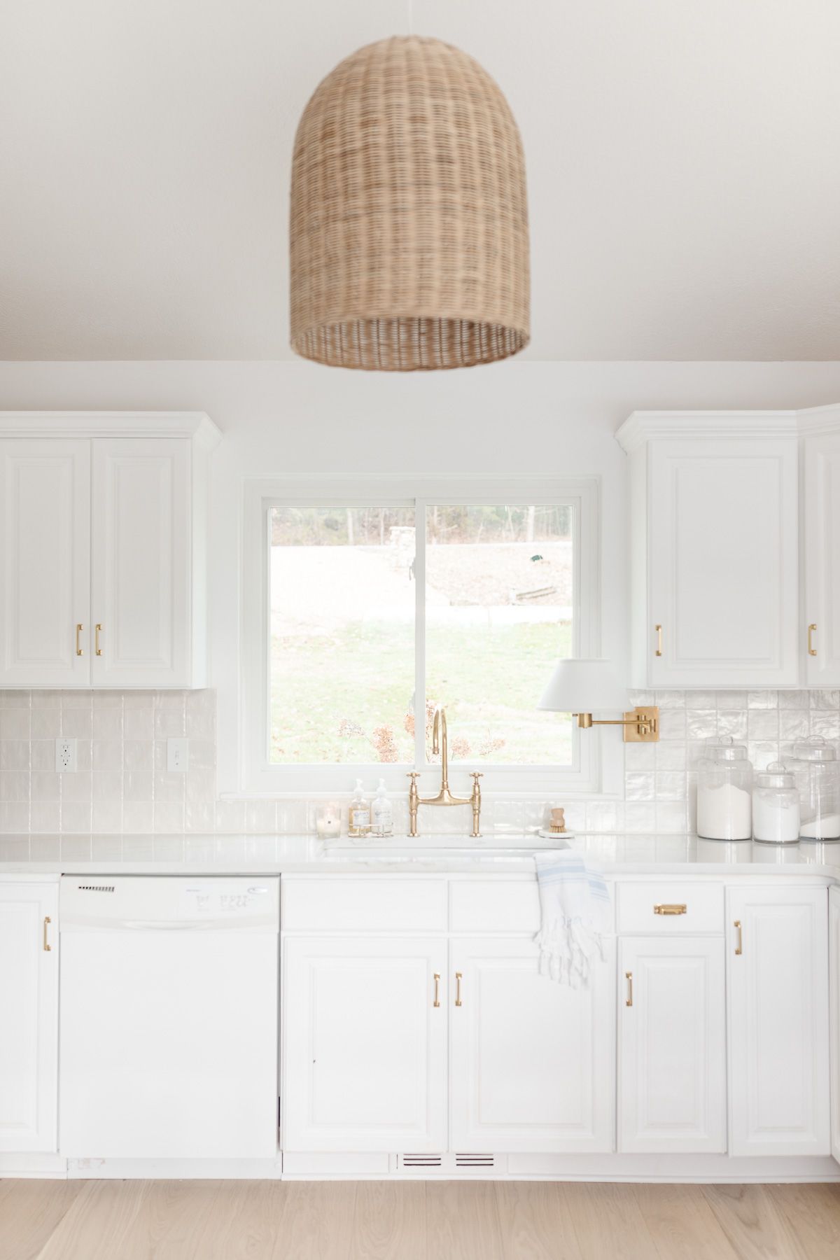 A white kitchen sink with brass faucet and organized countertops