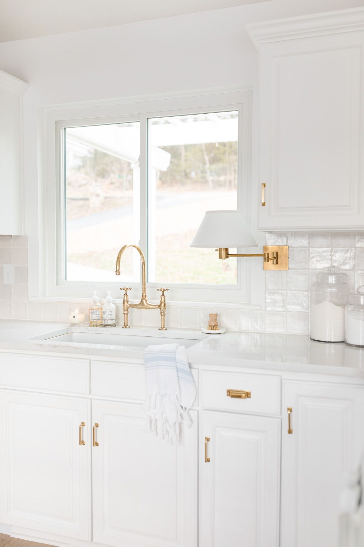 A white kitchen sink with brass faucet and organized countertops