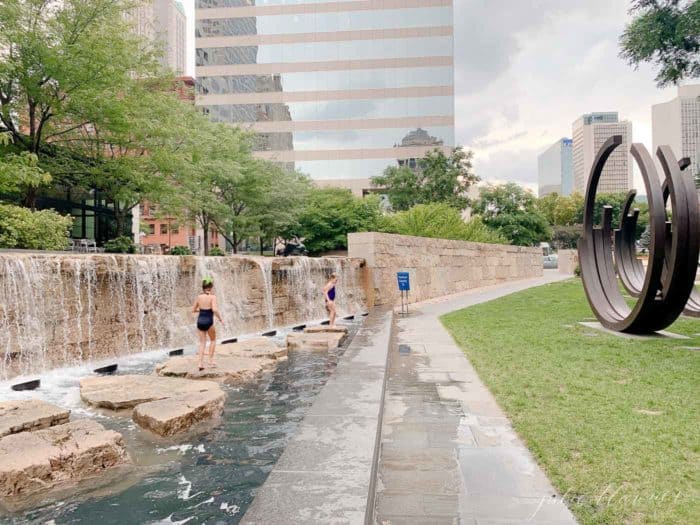 City scene with little girls skipping across rocks at a public fountain area.