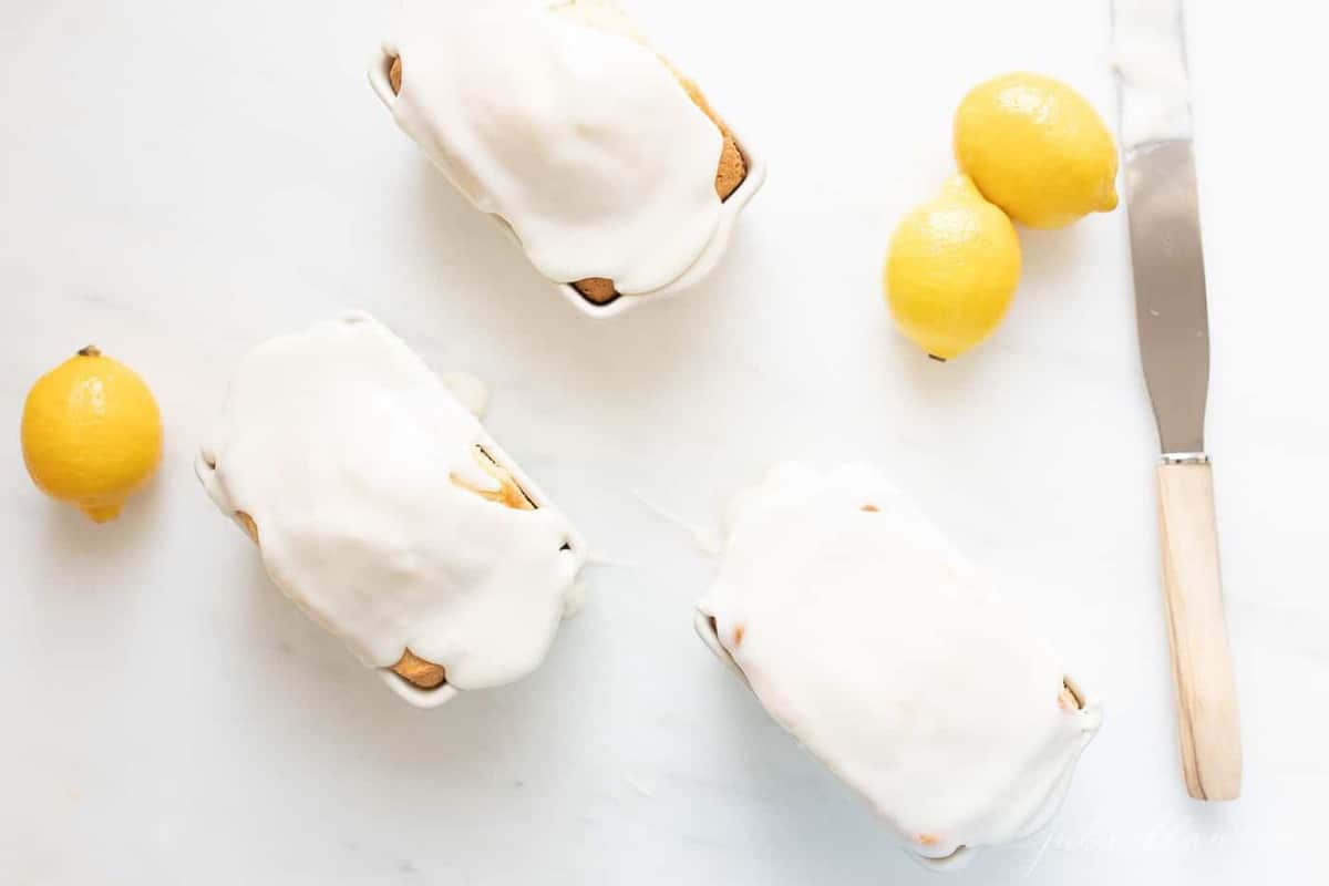 Three miniature loaves of lemon bread, meyer lemons to the side.