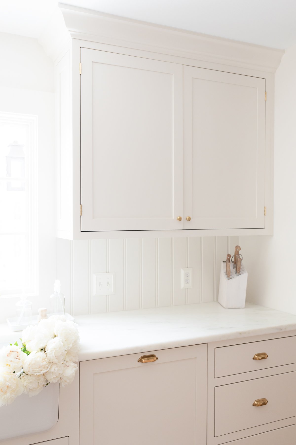 A minimalist kitchen with cream cabinets, marble countertops and white flowers in the sink.