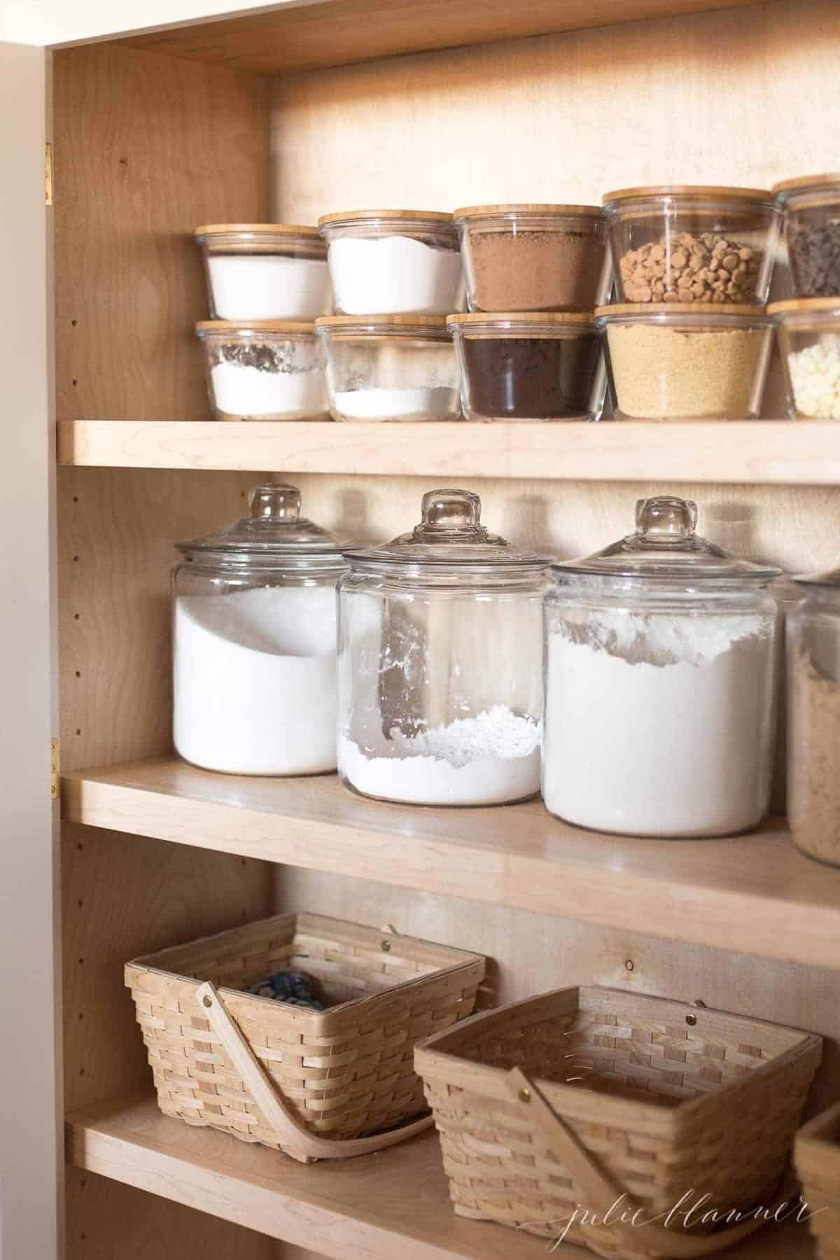 Looking into a pantry cabinet, clear jars and baskets storing food items.
