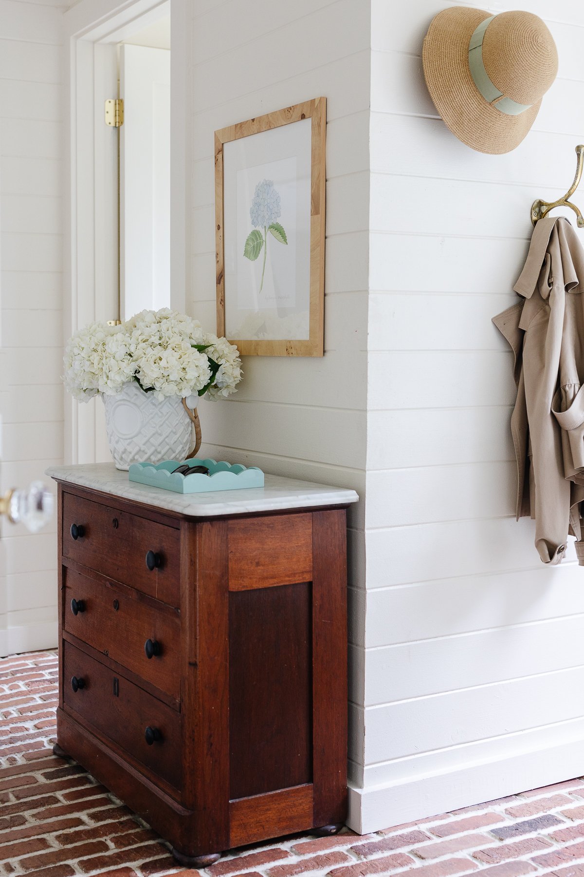 A white mudroom with brick floors and mudroom storage cabinet and hooks.