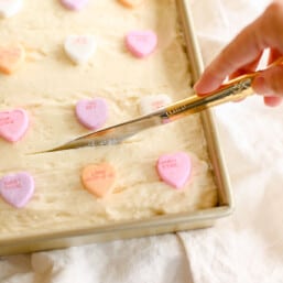 gold knife cutting sugar cookie bars with buttercream frosting