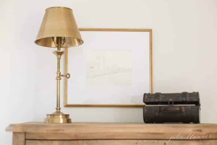 A wooden dresser with a piece of framed diy wall art, brass lamp.