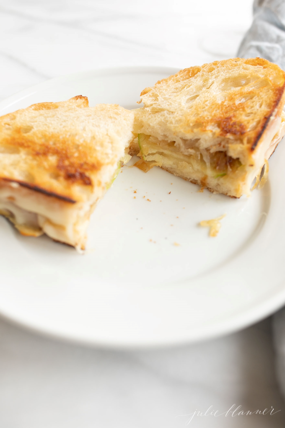 A gourmet grilled cheese on a white plate, cut into two.
