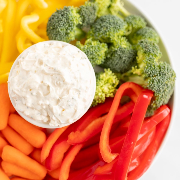 A white bowl full of veggie dip, surrounded by cut vegetables.