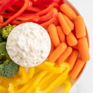 A white bowl full of vegetable dip, surrounded by cut vegetables.