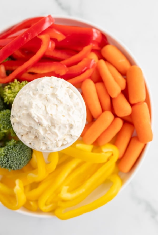 A white bowl full of vegetable dip, surrounded by cut vegetables.
