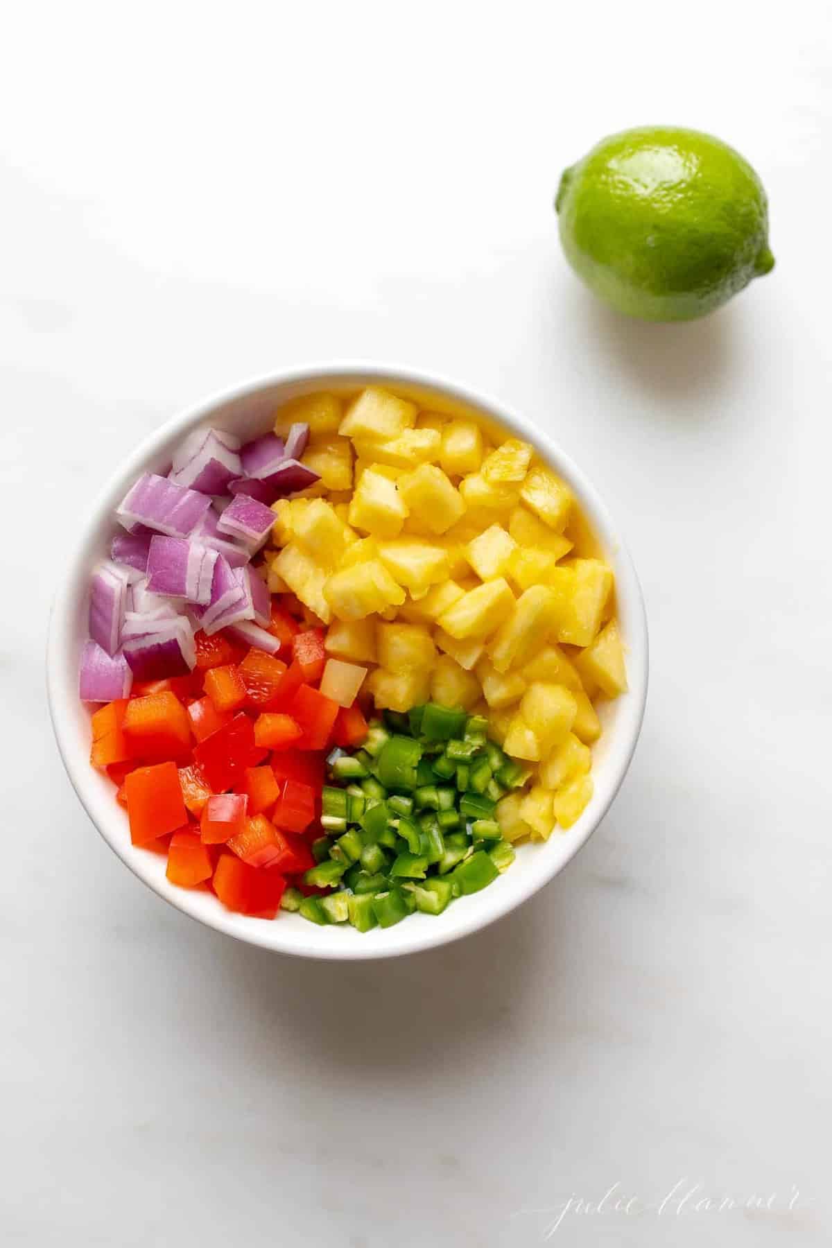 Pineapple salsa ingredients in a white bowl, with a lime to the side. 