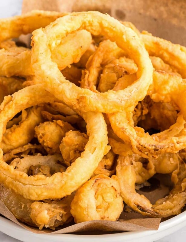 A white bowl of homemade onion rings, butcher paper lining the bowl.