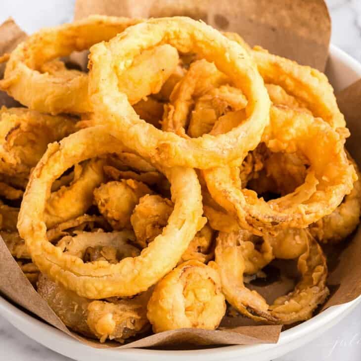 A white bowl of homemade onion rings, butcher paper lining the bowl.