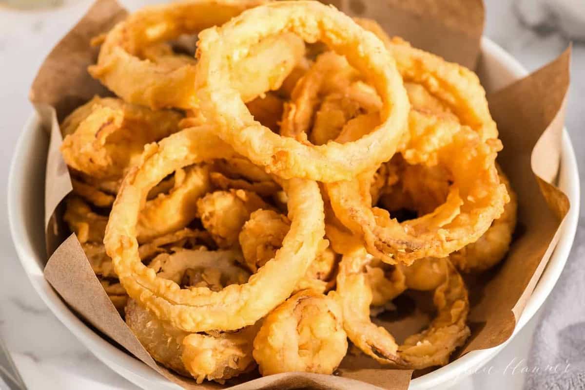 A white bowl of homemade onion rings, butcher paper lining the bowl.