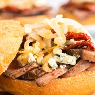 A steak sandwich with onion straws and cheese on top, top bun balanced to the side.