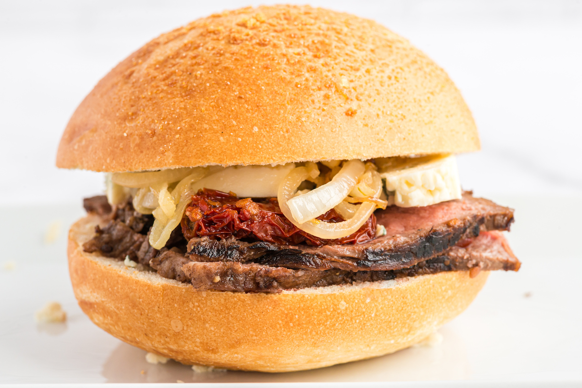 A delicious steak sandwich with beef and onions on a white plate.