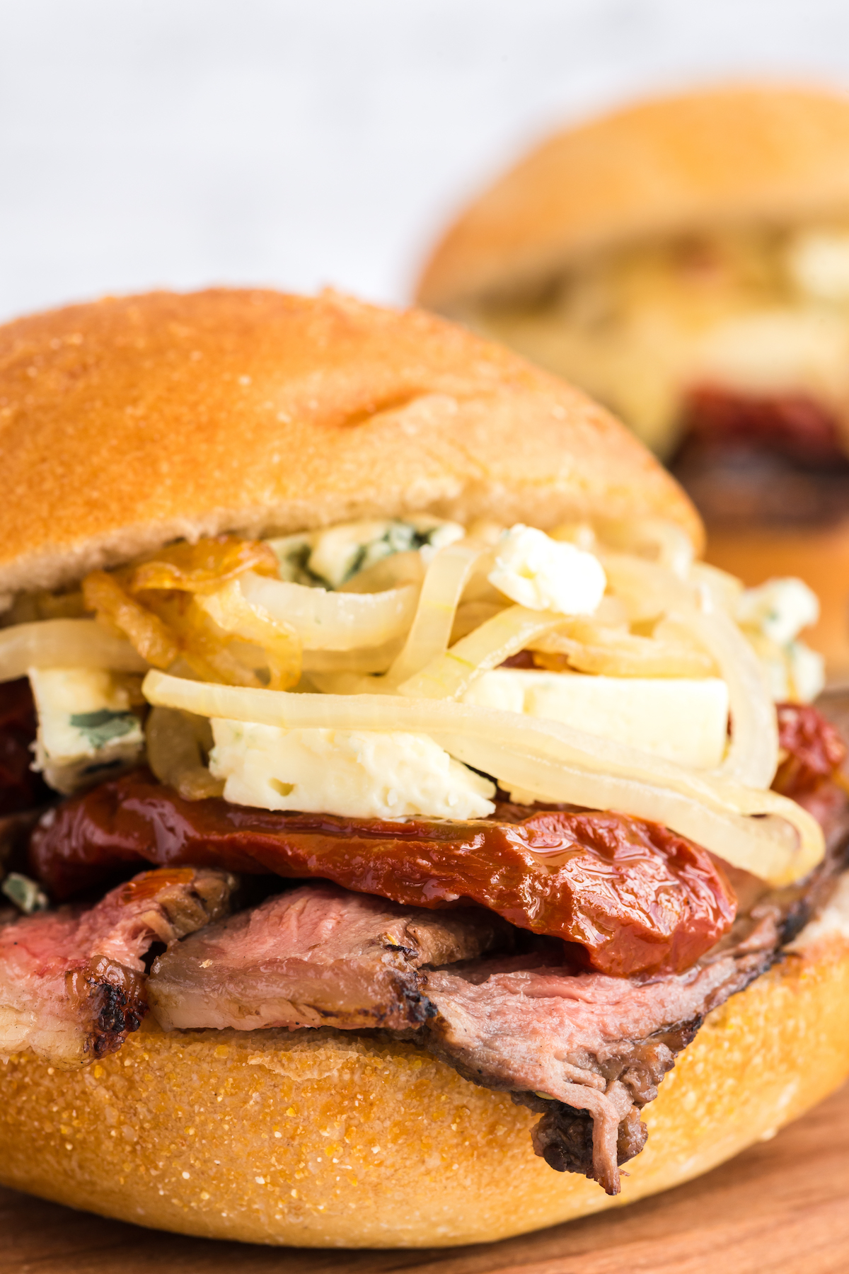 A mouthwatering steak sandwich piled high with juicy meat, caramelized onions, and melted cheese, served on a rustic wooden board.