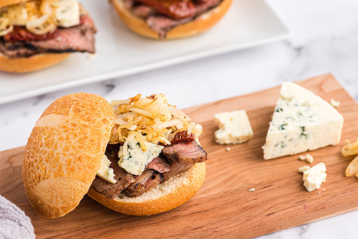 A mouthwatering steak sandwich with succulent slices of meat and melted cheese plated on a cutting board.