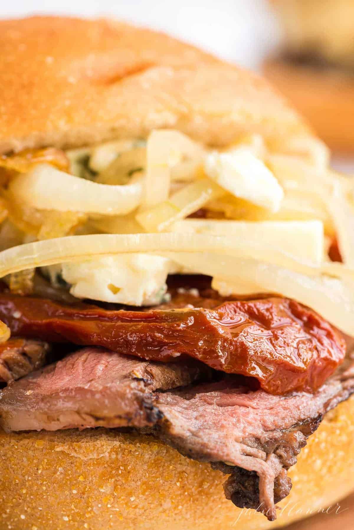 Close up of a steak sandwich on a bun, stacked with toppings.