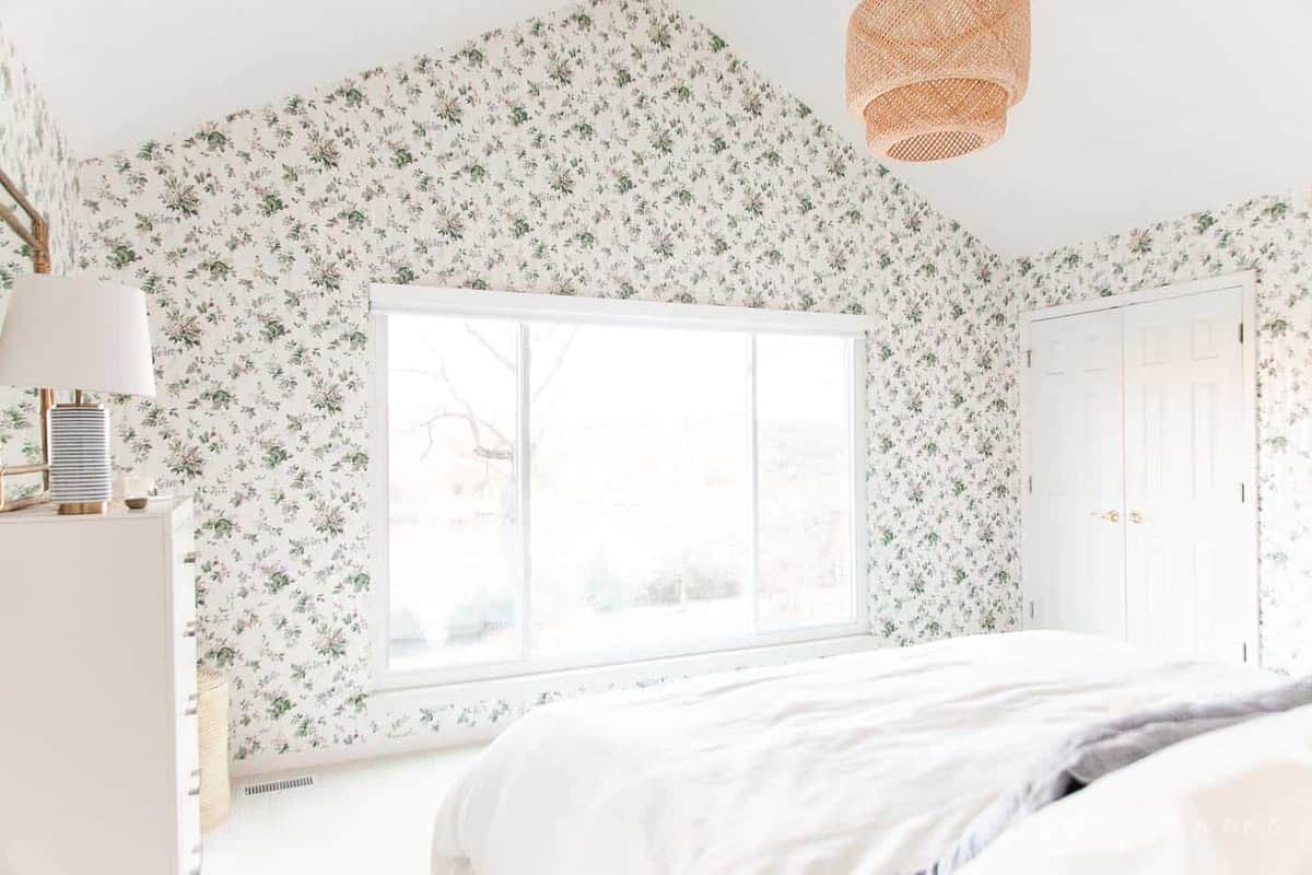 A white bedroom with wooden accents and a statement floral wallpaper. 