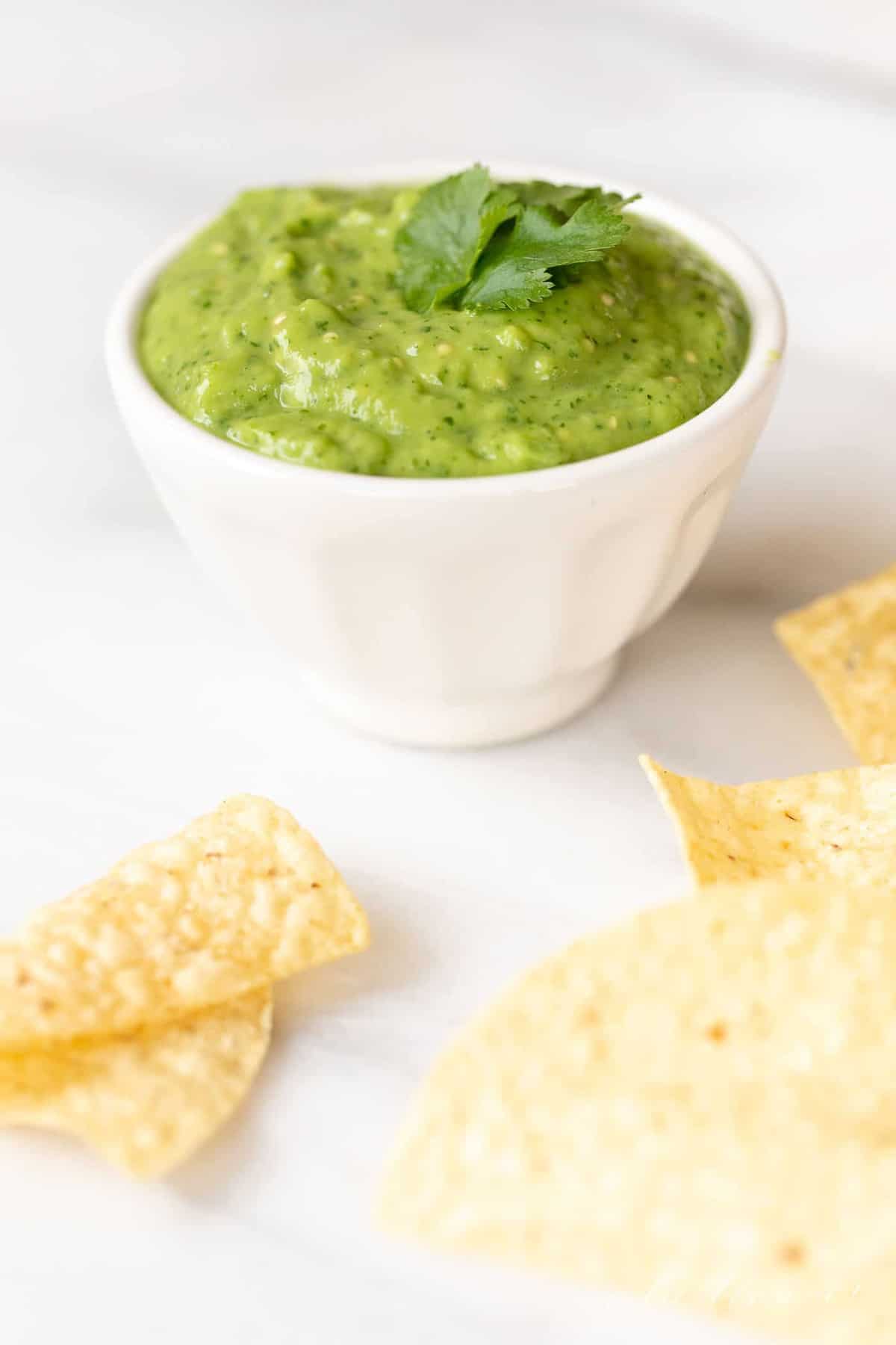 A white bowl of avocado sauce, tortilla chips scattered around.